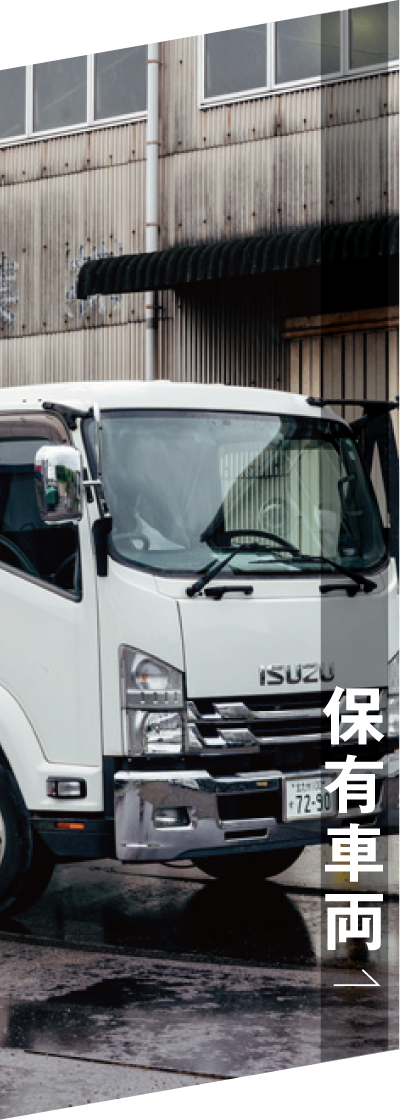 波板張りの工業用建物の前に停まっている白いいすゞのトラック。右側には日本語の文字が縦書きされている。.