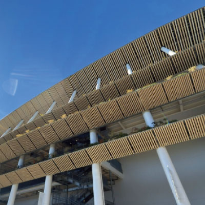 澄み切った青空を下から見下ろした、垂直の白い柱と水平の木製スラットが何段にも重なったモダンな建物。.