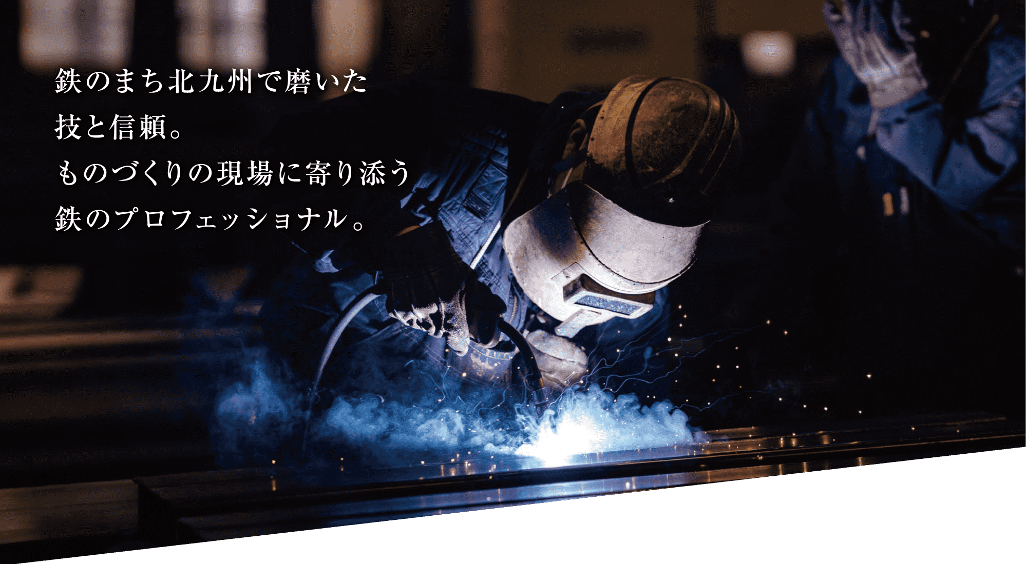 防護服を着用した人が、青い火花を散らしながら金属を溶接している。.