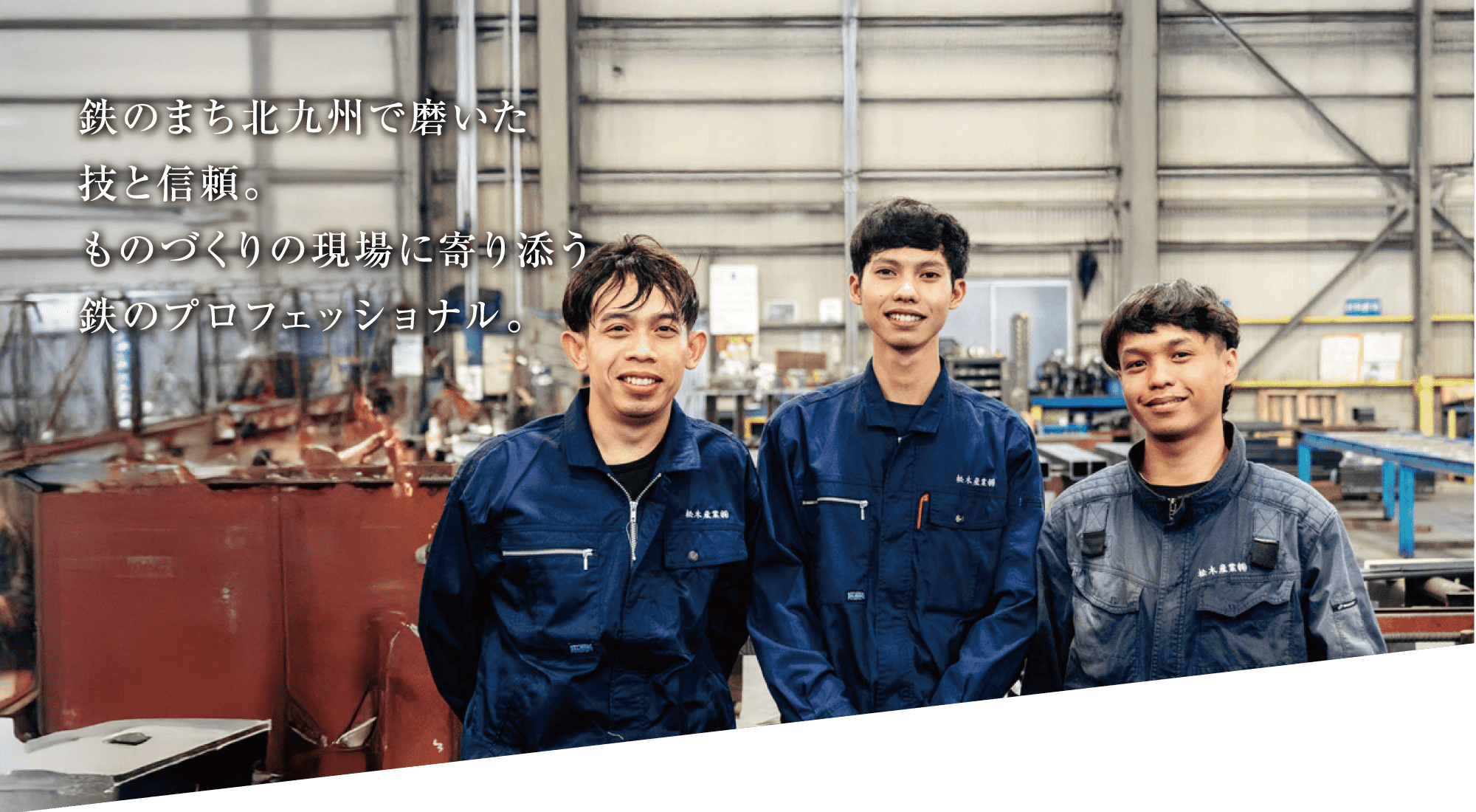金属製の構造物や設備を背景に、青い作業服を着た3人の男性が並んで立って微笑んでいる。画像左上には日本語のテキストが重ねられている。.